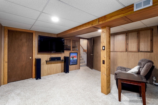 interior space with light carpet, a drop ceiling, and wood walls