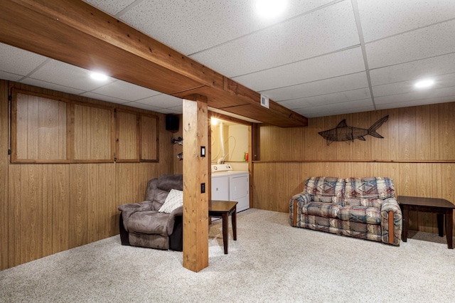 sitting room featuring light carpet, washer and clothes dryer, wooden walls, and a paneled ceiling