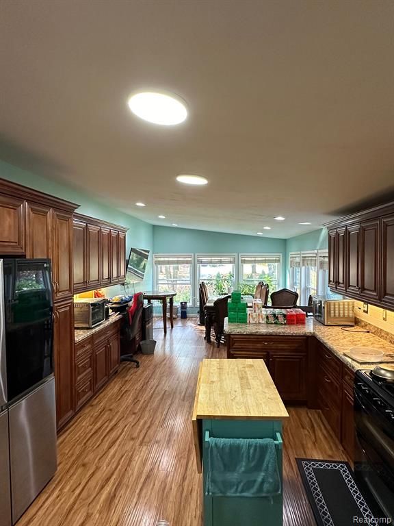 kitchen with hardwood / wood-style floors, stainless steel refrigerator, wood counters, kitchen peninsula, and black gas range