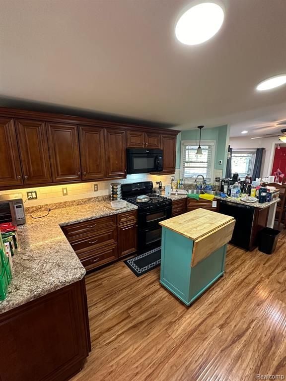 kitchen with hanging light fixtures, black appliances, light hardwood / wood-style floors, and kitchen peninsula