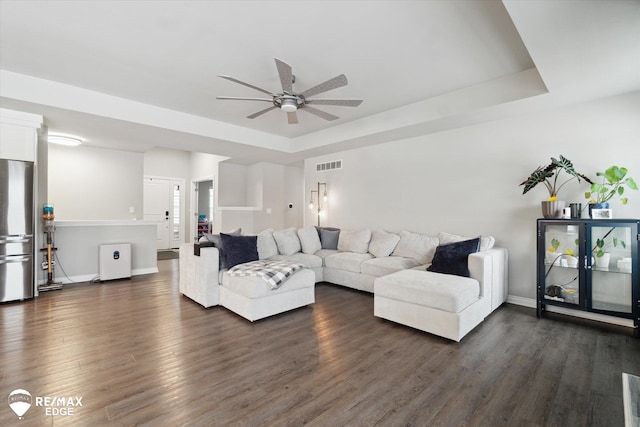 living room with ceiling fan, a tray ceiling, and dark hardwood / wood-style flooring