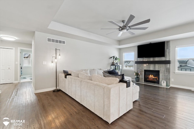 living room with a raised ceiling, a tiled fireplace, and dark wood-type flooring