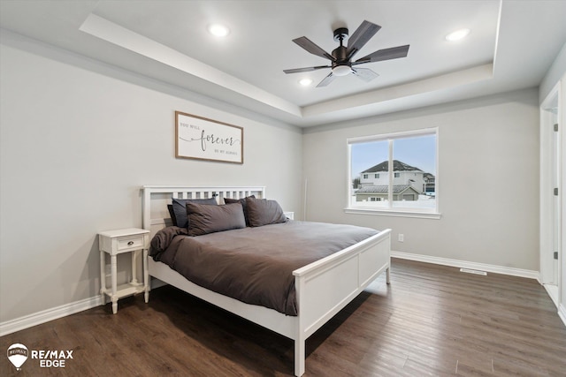 bedroom with dark hardwood / wood-style flooring, a tray ceiling, and ceiling fan