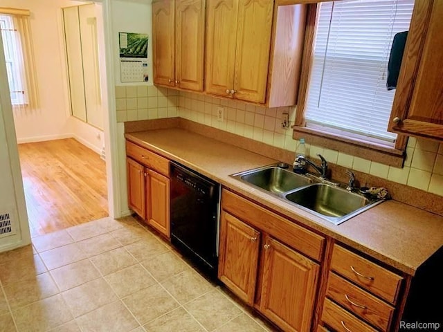 kitchen featuring black dishwasher, sink, decorative backsplash, and light tile patterned floors