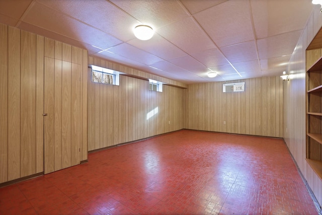 basement featuring a paneled ceiling and wooden walls