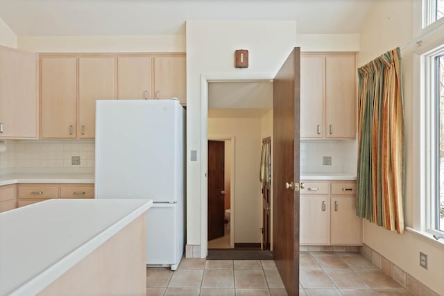 kitchen featuring light brown cabinetry, light tile patterned flooring, light countertops, freestanding refrigerator, and tasteful backsplash
