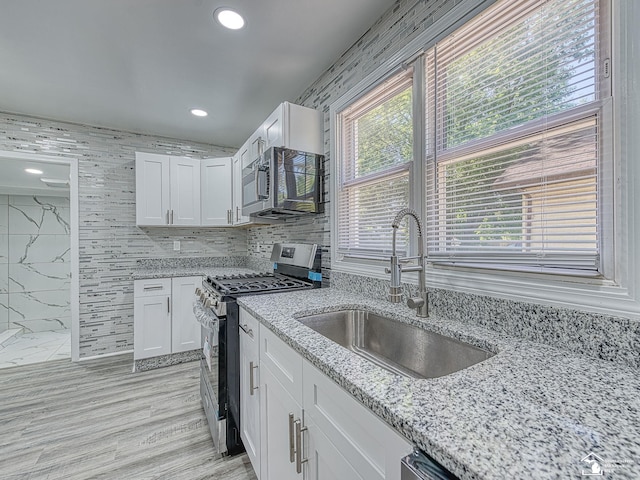 kitchen with appliances with stainless steel finishes, white cabinetry, sink, tile walls, and light stone countertops