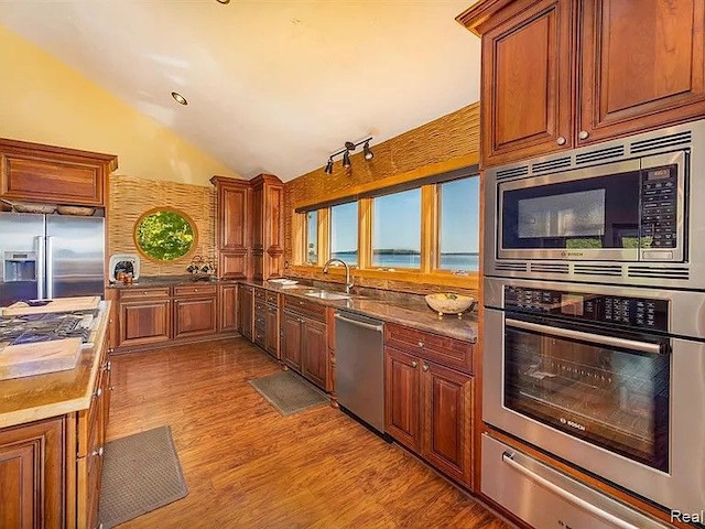 kitchen featuring vaulted ceiling, sink, light hardwood / wood-style floors, stainless steel appliances, and a water view