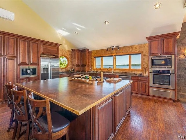 kitchen with a kitchen island, lofted ceiling, a breakfast bar area, built in appliances, and dark wood-type flooring