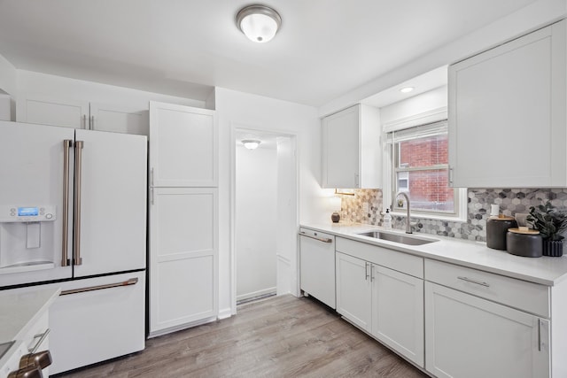 kitchen featuring white cabinetry, sink, backsplash, light hardwood / wood-style floors, and white appliances