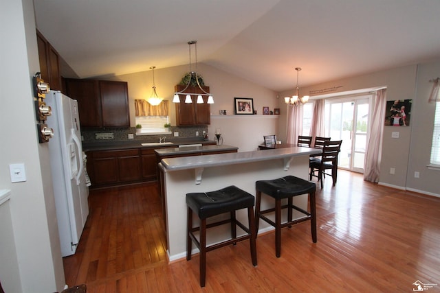 kitchen featuring pendant lighting, hardwood / wood-style floors, white refrigerator with ice dispenser, and a kitchen breakfast bar