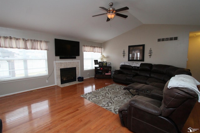 living room featuring lofted ceiling, light hardwood / wood-style flooring, a tile fireplace, and ceiling fan