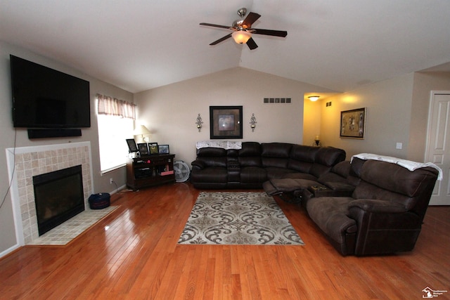 living room featuring a tiled fireplace, hardwood / wood-style floors, vaulted ceiling, and ceiling fan