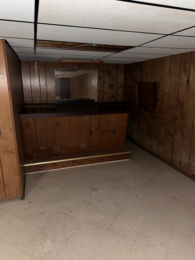 basement featuring a drop ceiling and wood walls