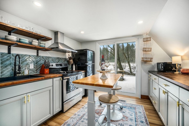 kitchen featuring stainless steel electric range oven, sink, wooden counters, light hardwood / wood-style floors, and wall chimney exhaust hood