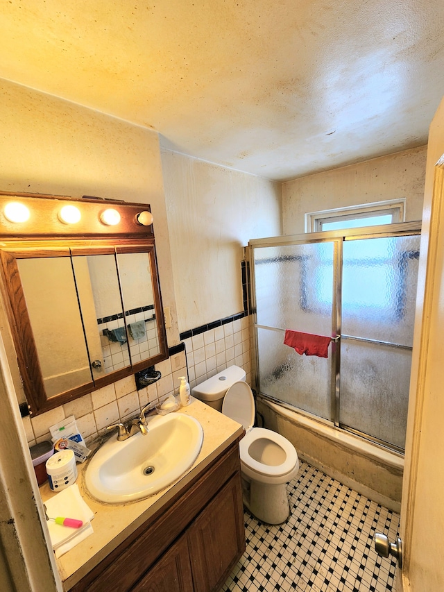 full bathroom with enclosed tub / shower combo, vanity, tile walls, and toilet