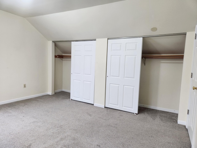 unfurnished bedroom with light carpet, two closets, and lofted ceiling