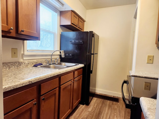 kitchen featuring black refrigerator, light hardwood / wood-style floors, sink, and electric range