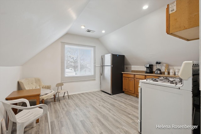 kitchen with lofted ceiling, stainless steel fridge, white range with gas stovetop, and light wood-type flooring