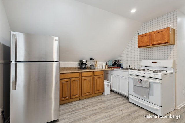 kitchen featuring white range with gas cooktop, vaulted ceiling, light hardwood / wood-style floors, and stainless steel refrigerator