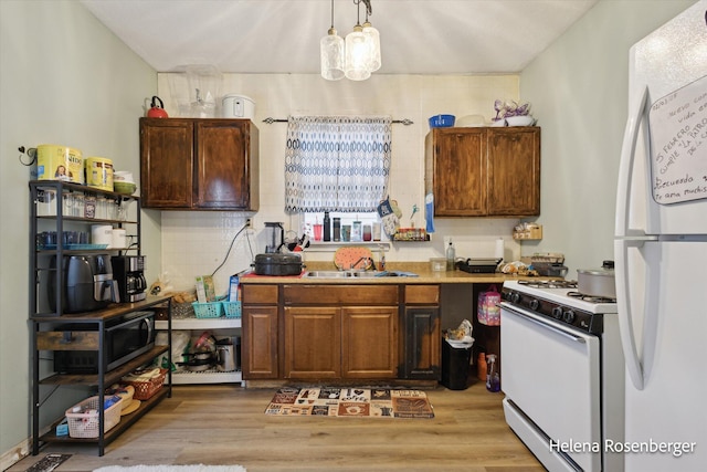 kitchen with pendant lighting, sink, white appliances, and light hardwood / wood-style flooring