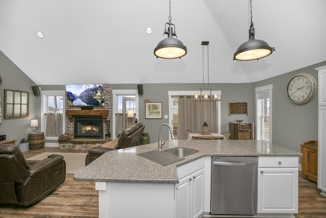 kitchen featuring white cabinetry, hanging light fixtures, stainless steel dishwasher, an island with sink, and a fireplace