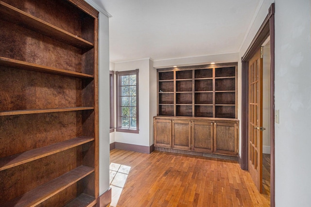 hallway featuring built in shelves, ornamental molding, and light wood-type flooring