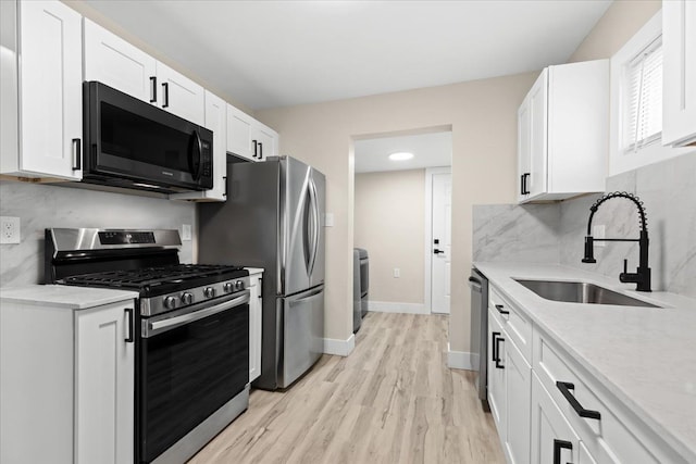 kitchen with appliances with stainless steel finishes, sink, white cabinets, decorative backsplash, and light hardwood / wood-style floors