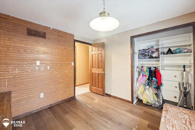 unfurnished bedroom with light hardwood / wood-style flooring, a closet, and wooden walls