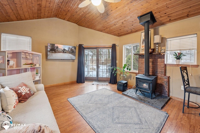 living room with wood ceiling, a wood stove, ceiling fan, vaulted ceiling, and light wood-type flooring