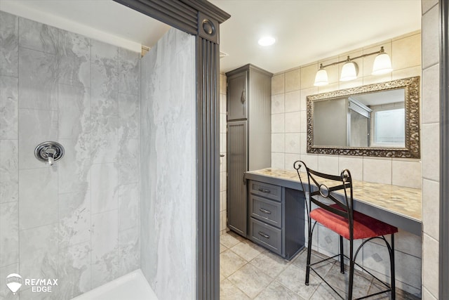 bathroom with tile walls, vanity, tile patterned flooring, and a tile shower