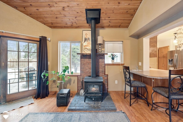 living room featuring vaulted ceiling, a wood stove, wood ceiling, and light hardwood / wood-style flooring