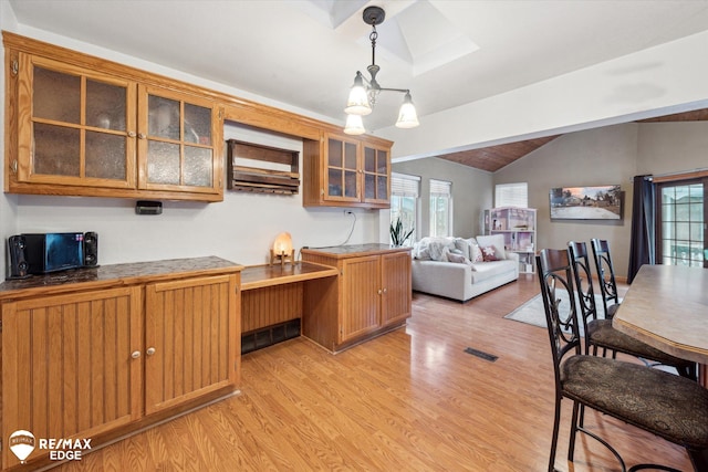 kitchen featuring vaulted ceiling with skylight, light wood-type flooring, and decorative light fixtures