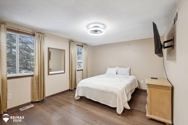 bedroom featuring multiple windows, dark hardwood / wood-style floors, and a textured ceiling