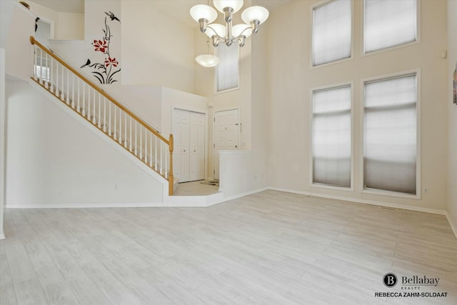 foyer entrance with an inviting chandelier, a towering ceiling, and light wood-type flooring