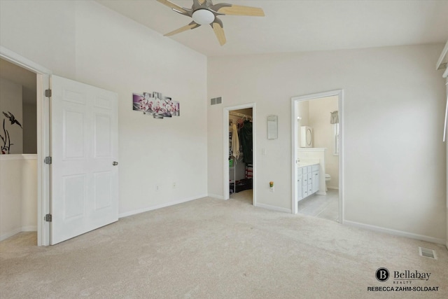 unfurnished bedroom featuring ensuite bath, high vaulted ceiling, light carpet, a spacious closet, and a closet