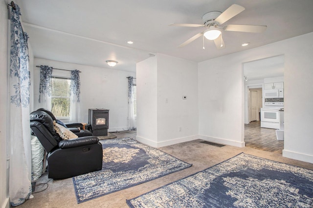 carpeted living room featuring ceiling fan and a wood stove