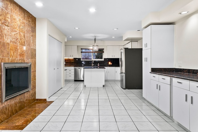 kitchen with a tile fireplace, appliances with stainless steel finishes, light tile patterned flooring, white cabinetry, and backsplash