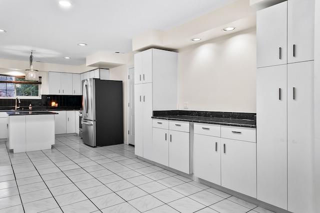 kitchen with white cabinetry, tasteful backsplash, a center island, stainless steel fridge, and dark stone counters