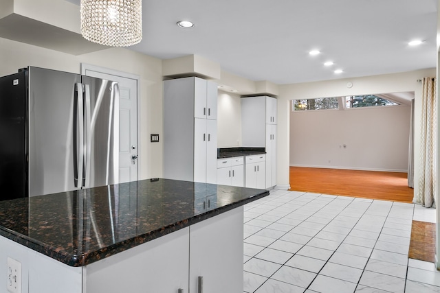 kitchen featuring stainless steel refrigerator, white cabinetry, dark stone countertops, and light tile patterned floors