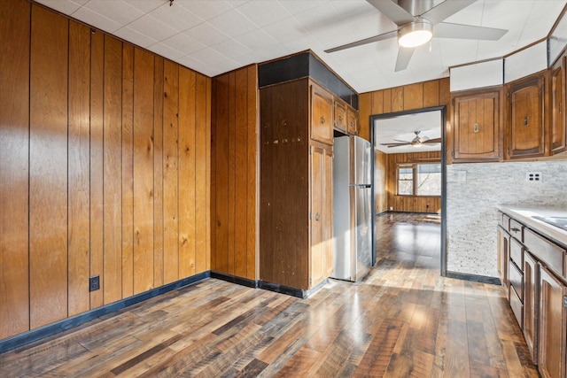 kitchen with hardwood / wood-style flooring, ceiling fan, stainless steel fridge, and wood walls