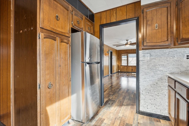 kitchen featuring light hardwood / wood-style flooring, stainless steel refrigerator, ceiling fan, and wood walls