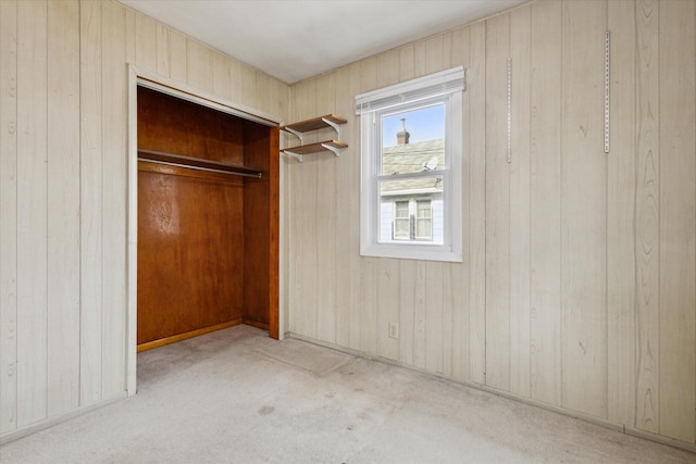 unfurnished bedroom with light carpet, a closet, and wood walls