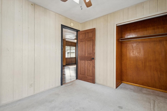 unfurnished bedroom with light carpet, a closet, ceiling fan, and wood walls