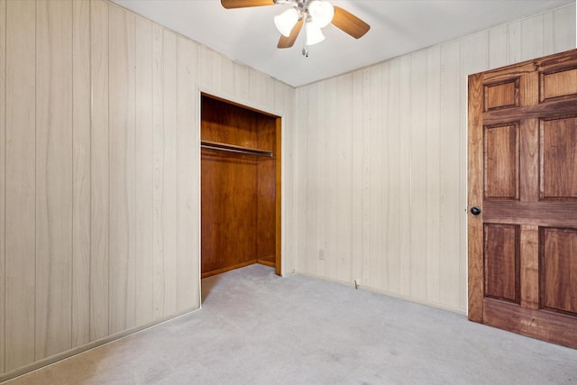 unfurnished bedroom with wooden walls, light colored carpet, and ceiling fan