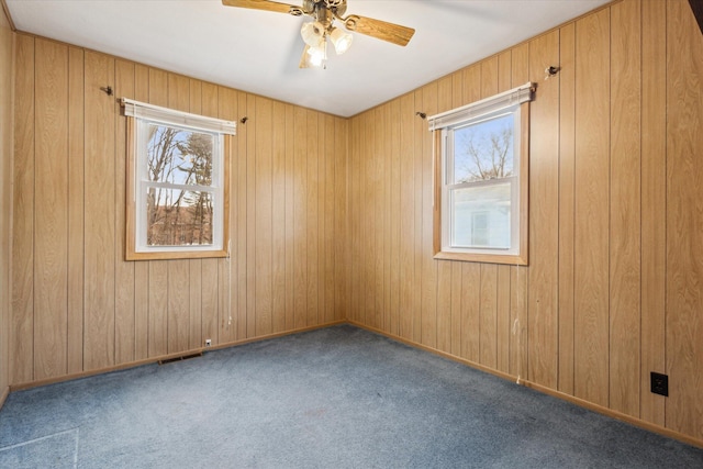 empty room featuring wood walls, ceiling fan, and dark colored carpet