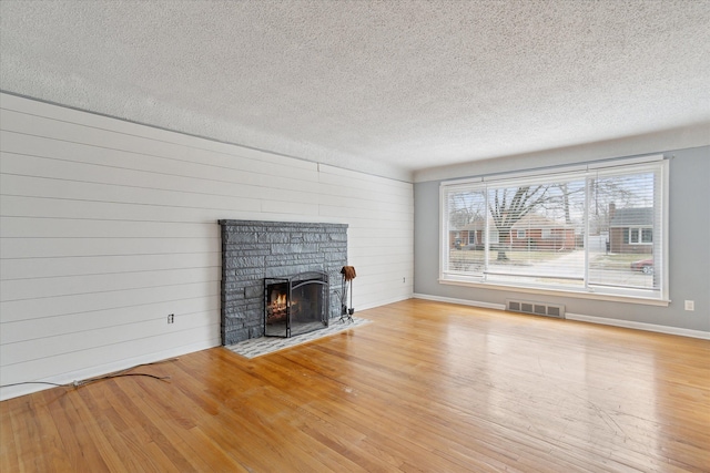 unfurnished living room featuring wood walls, a textured ceiling, a fireplace, and light hardwood / wood-style floors