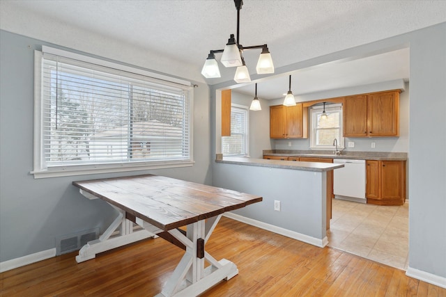 kitchen with light hardwood / wood-style flooring, dishwasher, a textured ceiling, decorative light fixtures, and kitchen peninsula