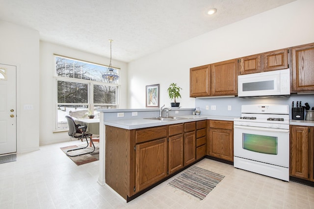 kitchen with sink, white appliances, decorative light fixtures, and kitchen peninsula