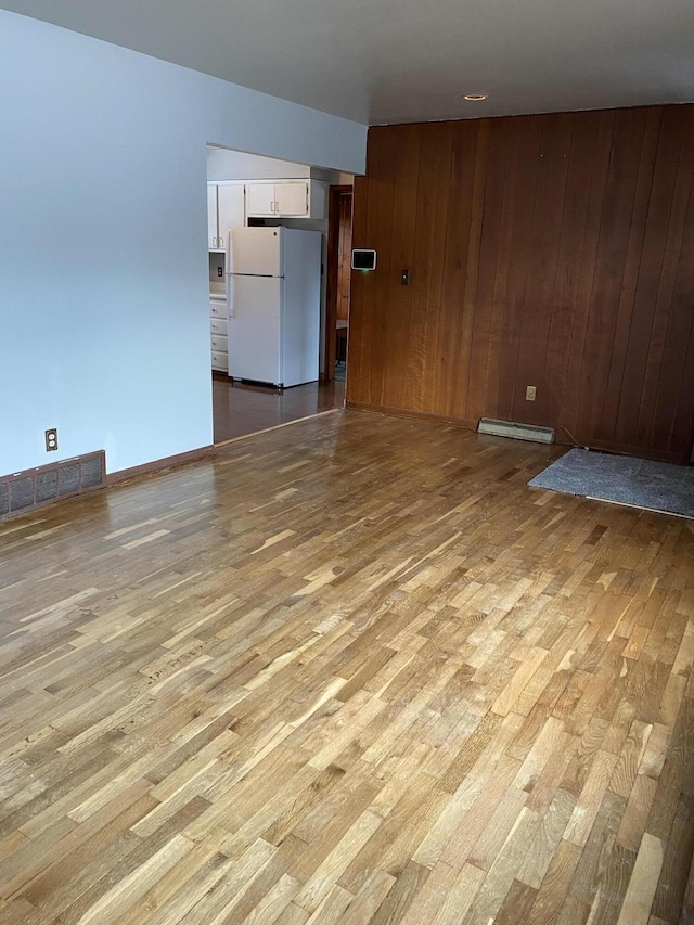 spare room featuring a baseboard radiator, wooden walls, and light wood-type flooring